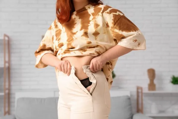 Image of woman trying to do her trousers up after pregnancy weight gain Whitnash