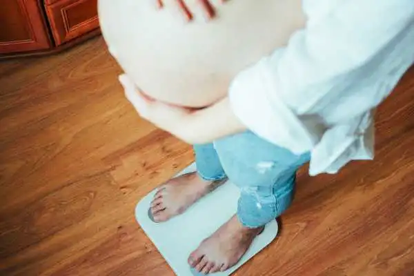Image of woman weighing herself and experiencing weight gain through pregnancy Whitnash